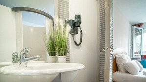 Et badeværelse med en hvid vask, et spejl, en telefon og en potteplante.