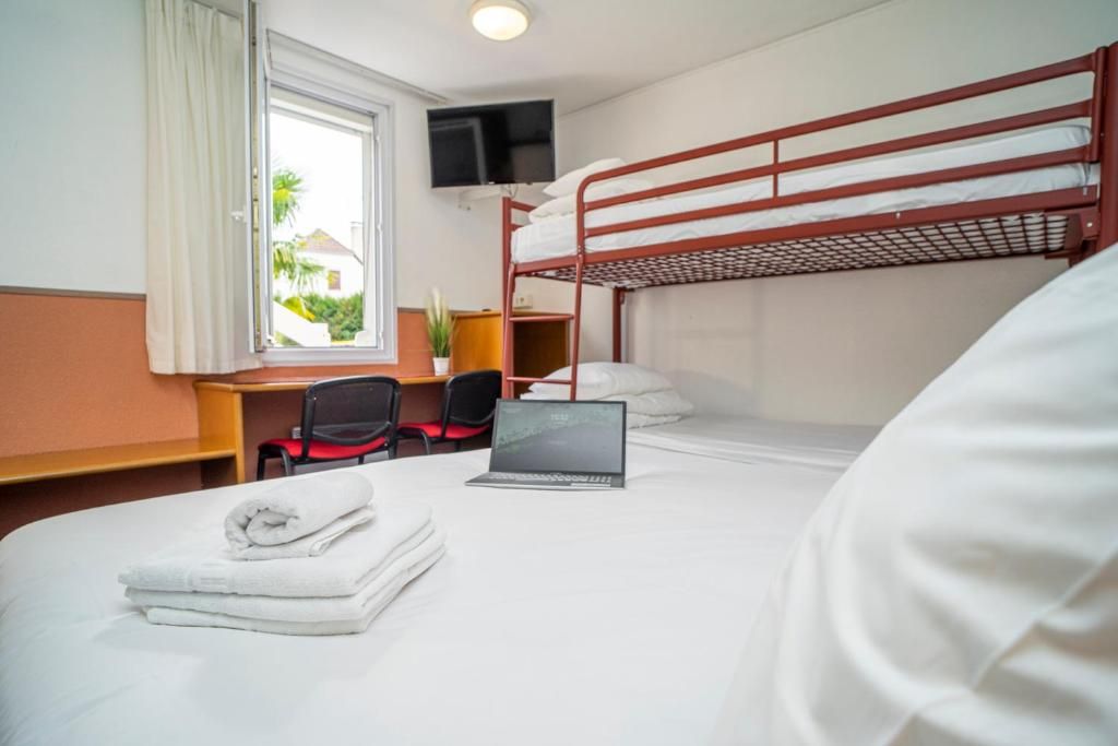 A hotel room with a bunk bed, a desk with a laptop, a chair, and a TV mounted on the wall.