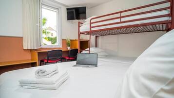 A hotel room with a bunk bed, a desk with a laptop, a chair, and a TV mounted on the wall.