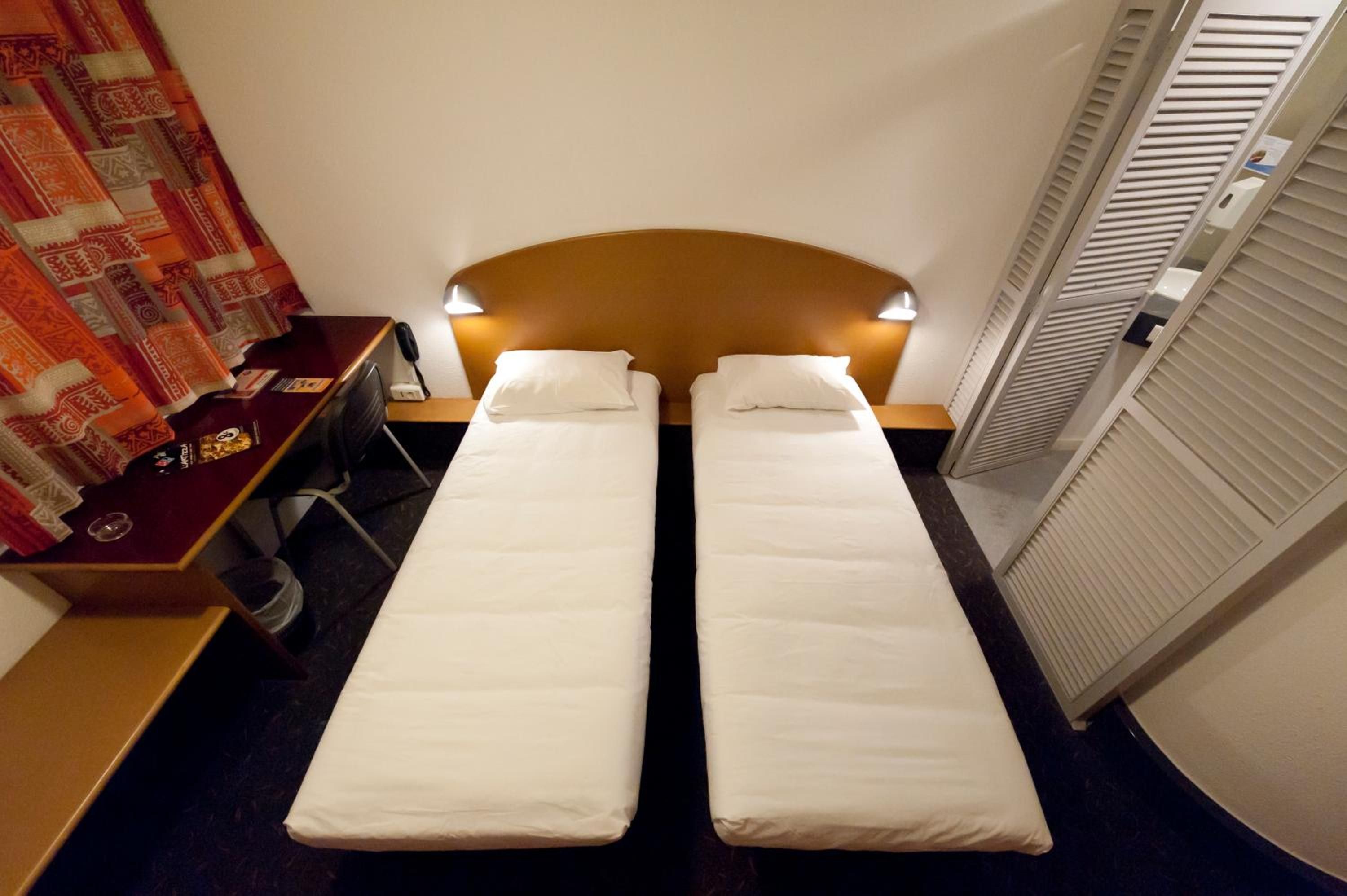 Habitación doble con dos camas individuales, un escritorio con silla, una mesita y una cortina.
