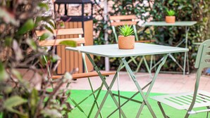 En hyggelig udendørs terrasse med et bord og stole, omgivet af grønne planter.