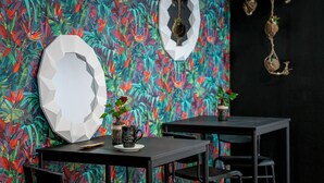Et værelse med sprudlende tropisk tapet, et hvidt geometrisk spejl, en kaffekop og en lille potteplante.