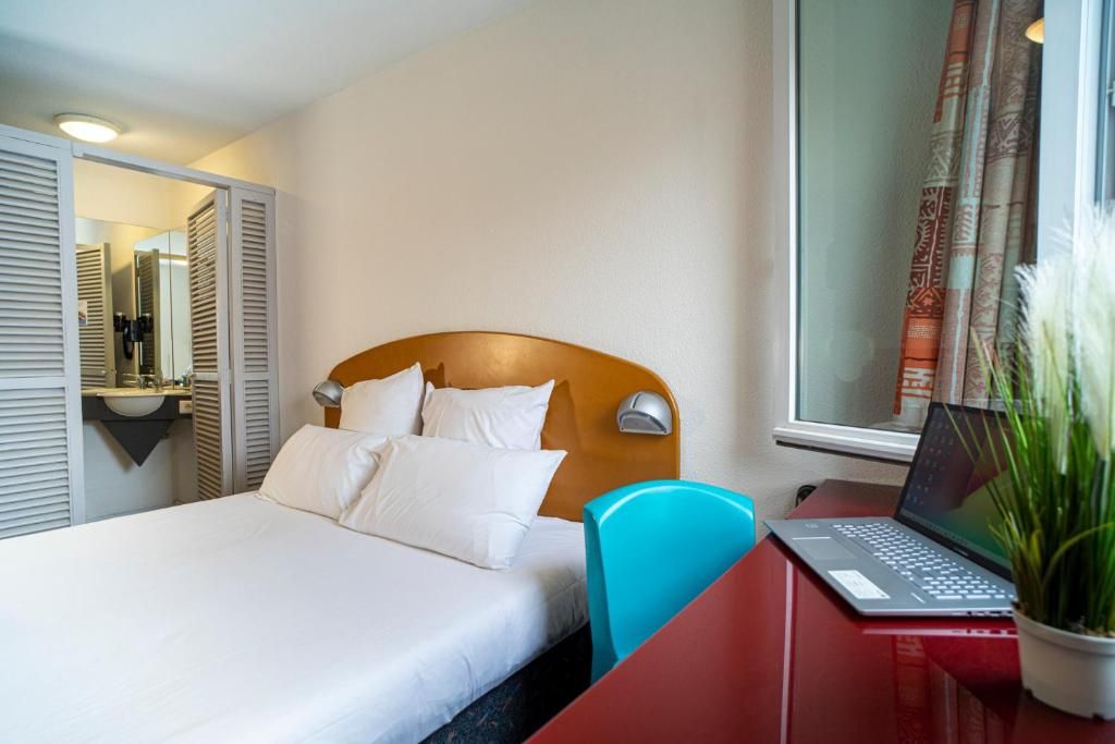 Habitación de hotel con cama, escritorio con una computadora portátil, una silla y una planta en maceta.
