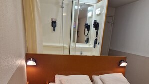 A hotel room with a bed, a nightstand, a mirror, and a shower area. - Quick Palace Vannes (Vannes)
