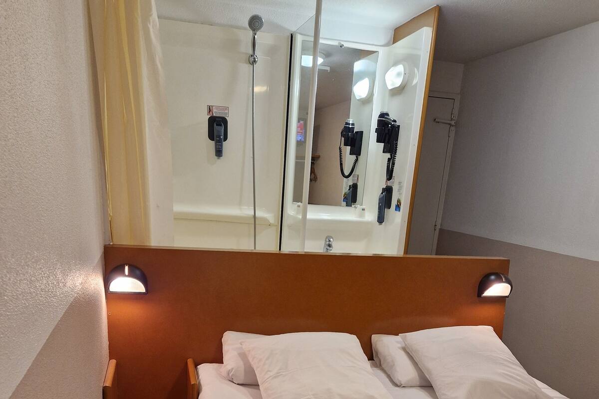 Une chambre d’hôtel comprenant un lit, une table de chevet, un miroir et un espace douche.
