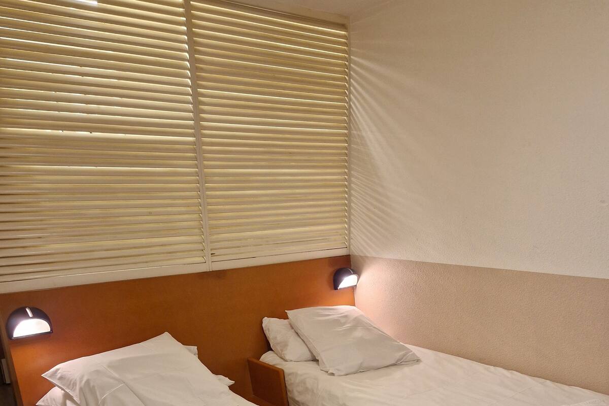Une chambre d’hôtel avec deux lits simples, chacun doté de draps et d’oreillers blancs, d’une tête de lit et d’une lampe de lecture fixée au mur.