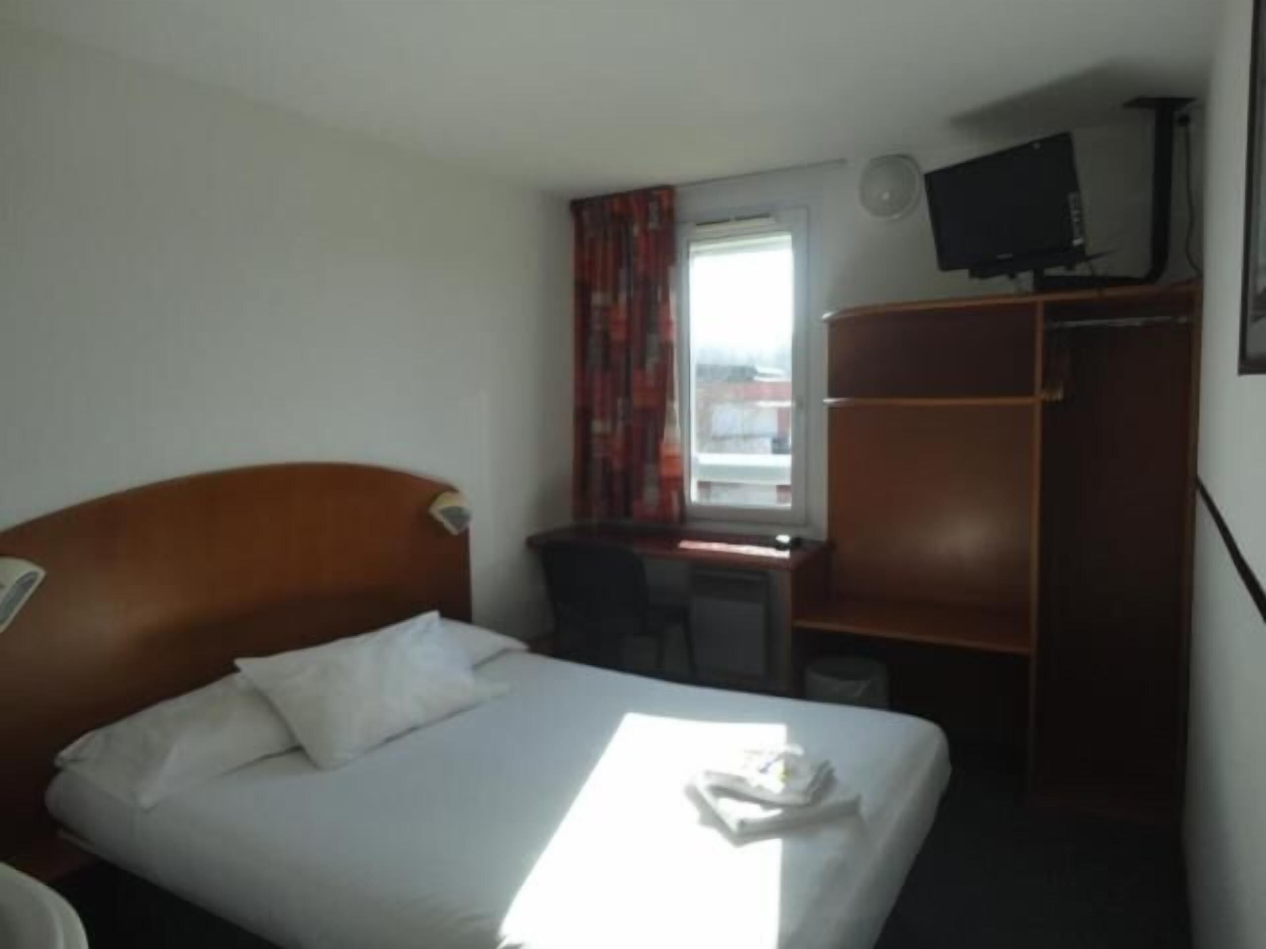Een hotelkamer met een bed, een bureau, een kledingkast en een televisie.