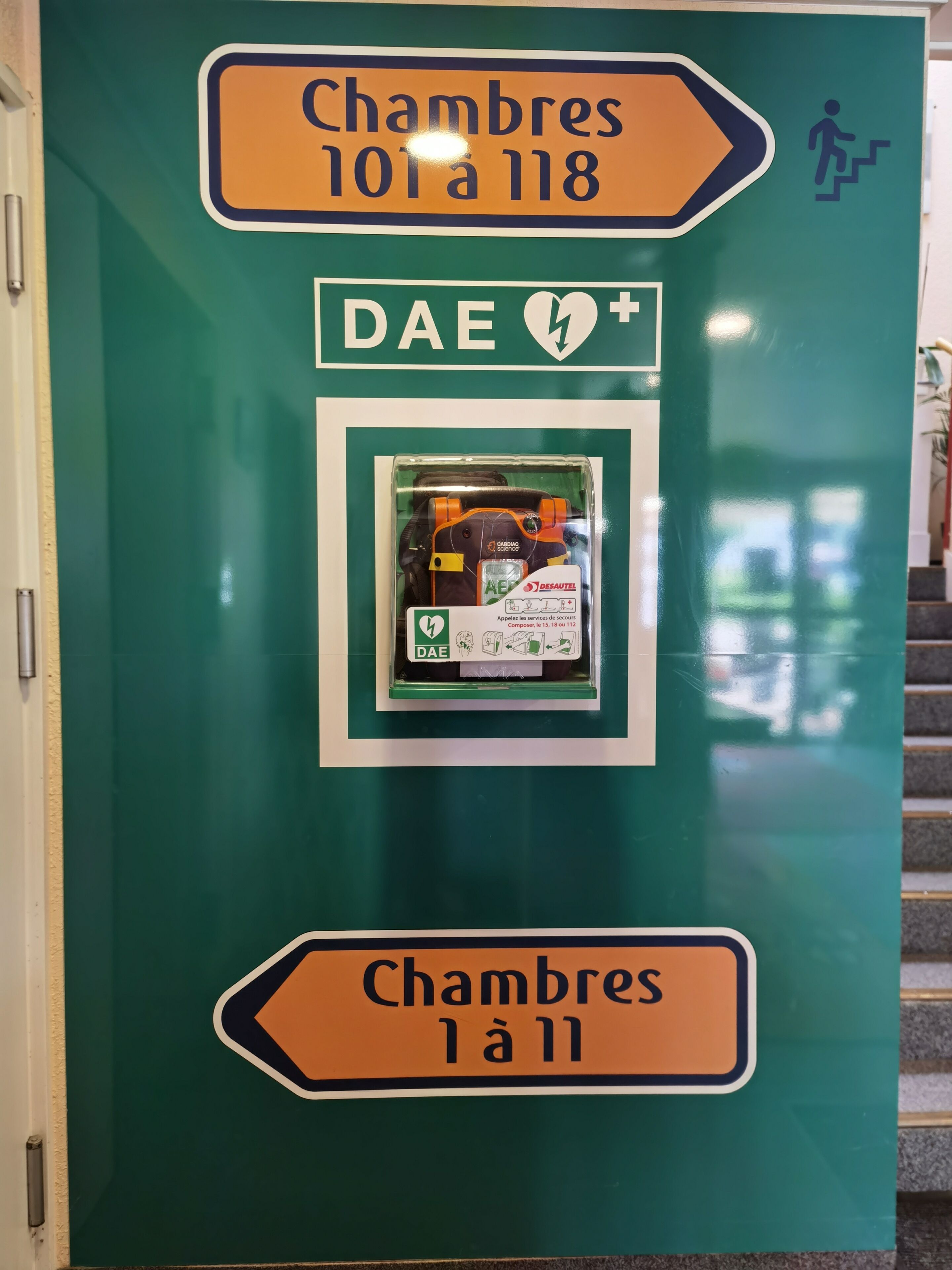 Ein grünes Schild mit Pfeilen und Notfallkontaktdaten.