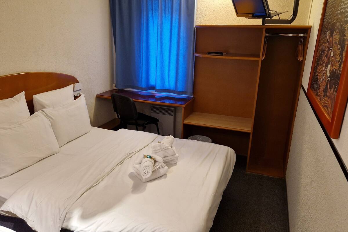 A hotel room with a bed, a desk, a chair, and a small shelf.
