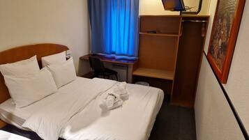 A hotel room with a bed, a desk, a chair, and a small shelf.