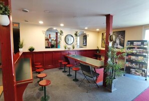 Un restaurante con una barra larga, taburetes rojos y una estantería con revistas.