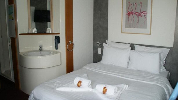 A hotel room with a bed, white linens, a round sink, a mirror, and a framed picture of flamingos on the wall. - Quick Palace Epinal (Epinal)
