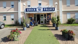 A hotel named "Quick Hotel Palace" with a signboard, outdoor seating area, and potted plants. - Quick Palace Epinal (Epinal)