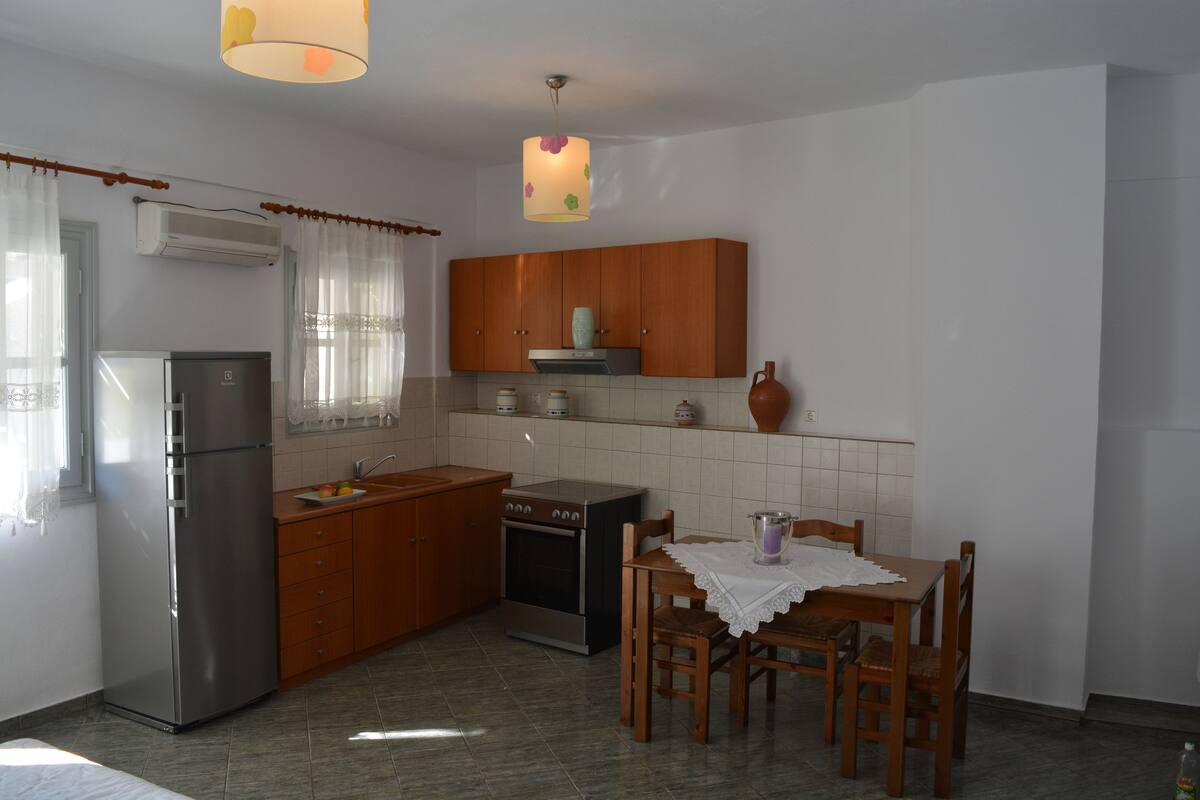 A compact kitchen with a refrigerator, stove, wooden cabinets, and a dining table with chairs.