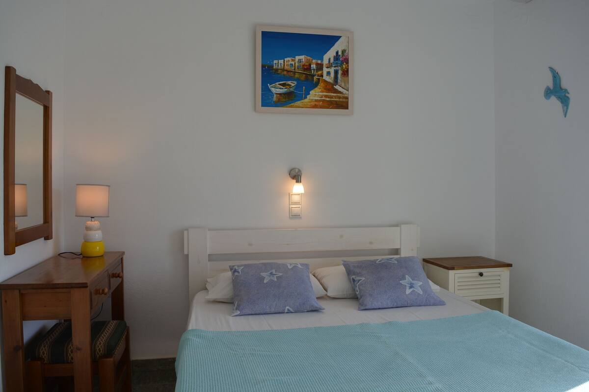 A bedroom with a bed, bedside table, lamp, and a painting on the wall.