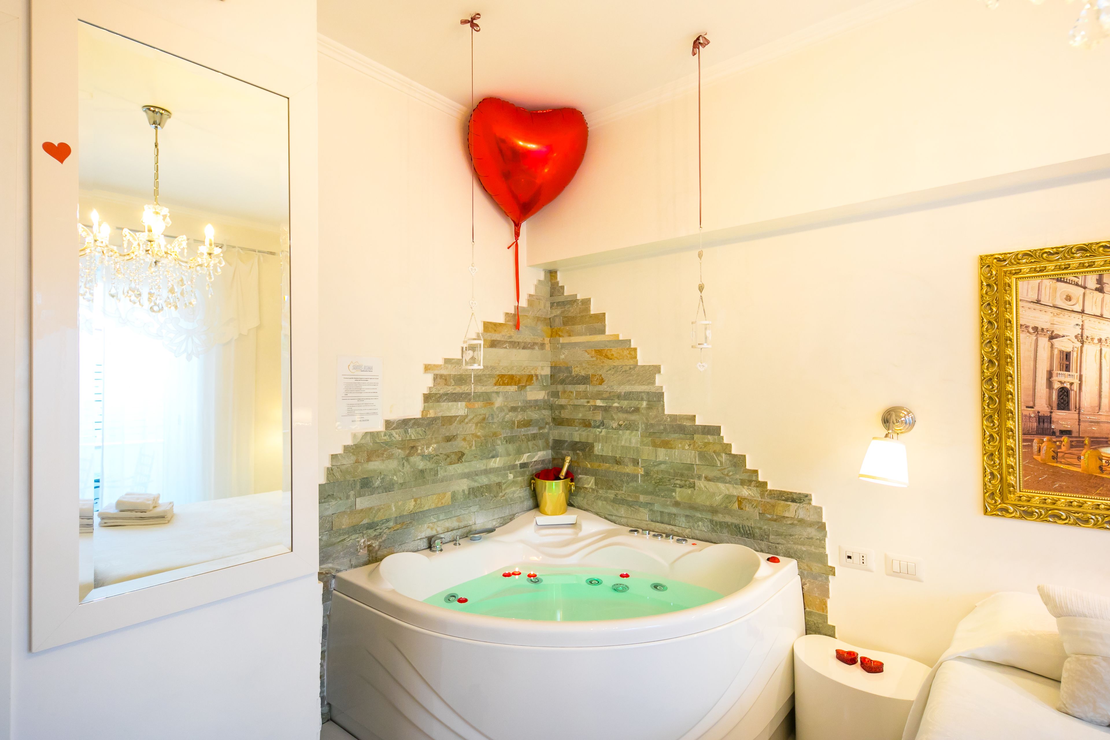Un baño con una bañera grande, un espejo, una araña y un globo con forma de corazón.