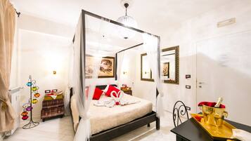 A four-poster bed with a canopy, a bedside table with a tray holding a champagne bottle and glasses, and a mirror on the wall.