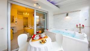 Una habitación con una bañera blanca, una mesa de comedor con alimentos para el desayuno, y vistas a una habitación amarilla a través de una puerta corrediza.