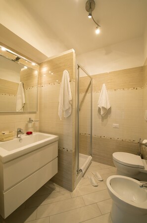 A modern bathroom with a glass shower enclosure, a sink, a bidet, and a toilet. - Suites Roma Tiburtina (Rome)