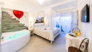Un dormitorio con una bañera curva, una cama con dosel, una mesa de comedor con una botella de champán y un globo con forma de corazón.