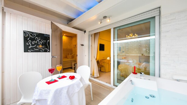 Una habitación con una mesa blanca, dos sillas, un separador de vidrio, una bañera y una puerta que da a otra habitación.