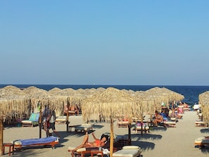 A beach with rows of sunbeds and thatched umbrellas, a clear sky, and the sea in the background. - Blue Beach Studios (Constanta)