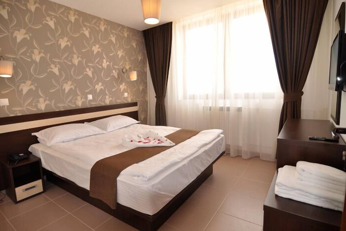 Ein Hotelzimmer mit einem großen Bett, einem Nachttisch mit Lampe, einem Fernseher und einem Badebereich mit Handtuchhalter.