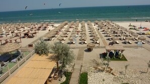 Une plage bordée de rangées de chaises longues et de parasols, une terrasse en bois et une vue dégagée sur la mer.