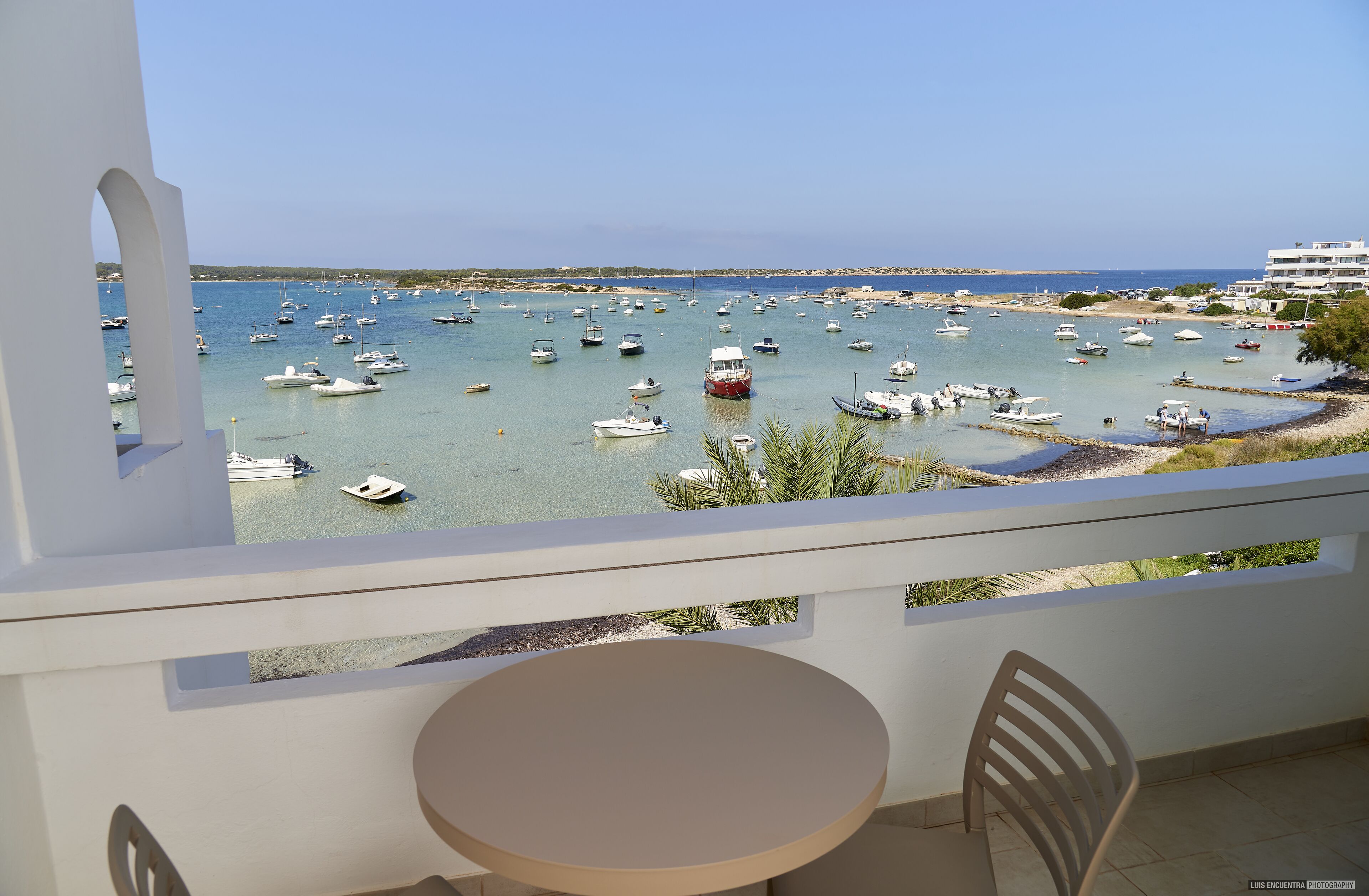 Un balcon avec une table et des chaises donnant sur une marina où sont amarrés de nombreux bateaux.
