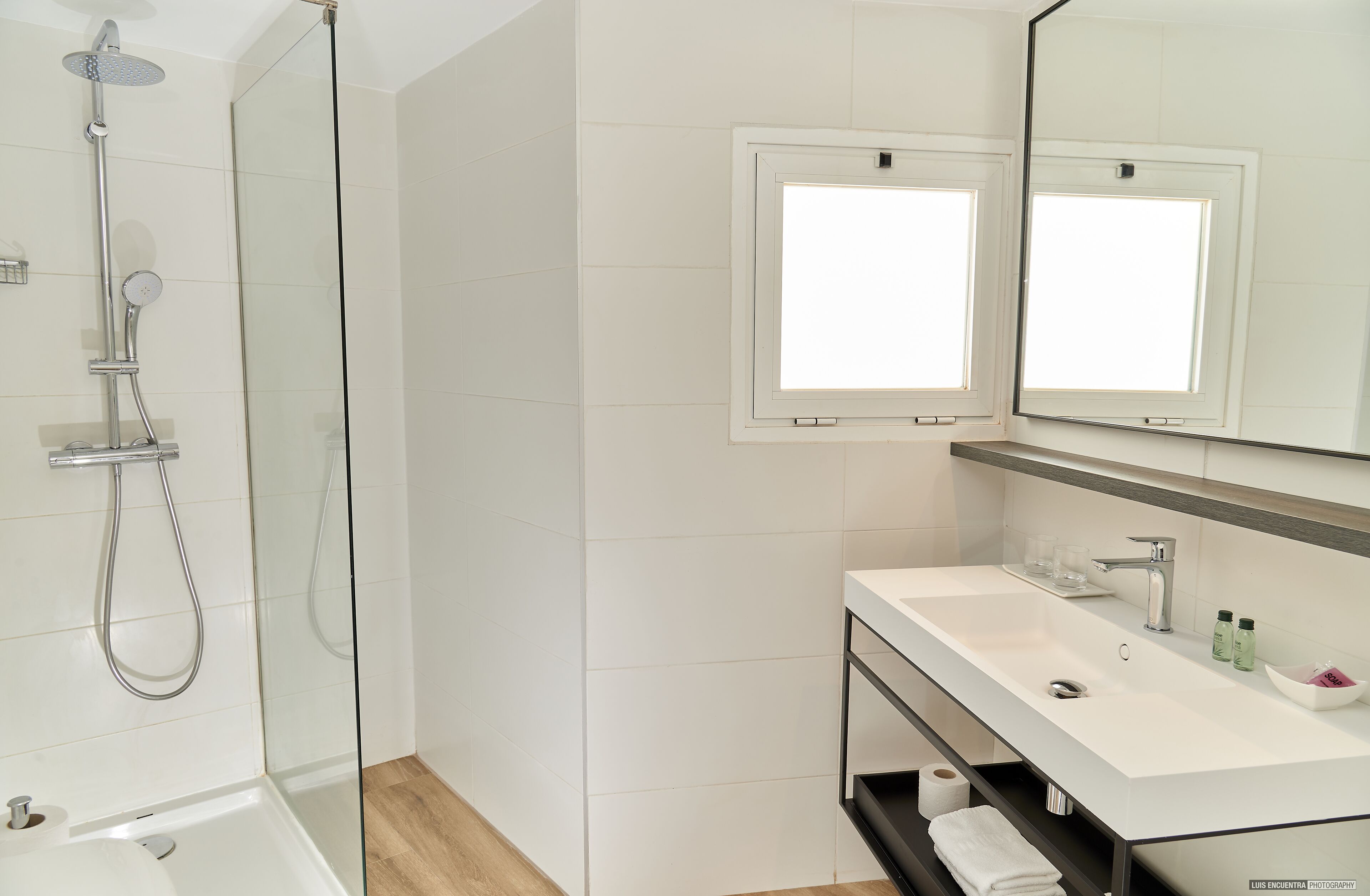 Un bagno moderno con cabina doccia in vetro, un lavandino bianco con specchio sopra e uno scaffale con articoli da toilette.