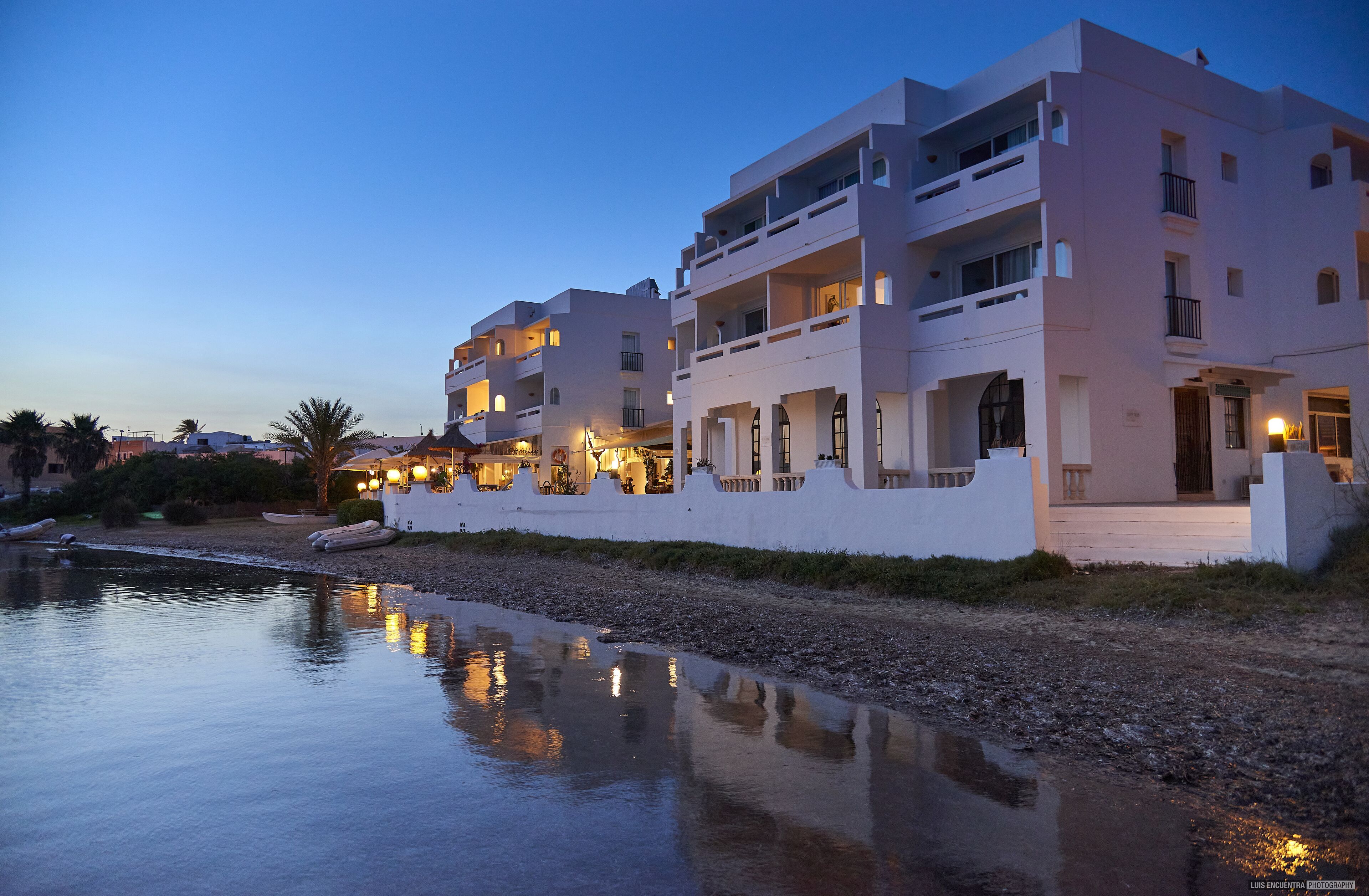 Un hotel frente al agua con varios balcones, piscina e iluminación exterior.