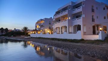 Un hotel frente al agua con varios balcones, piscina e iluminación exterior.