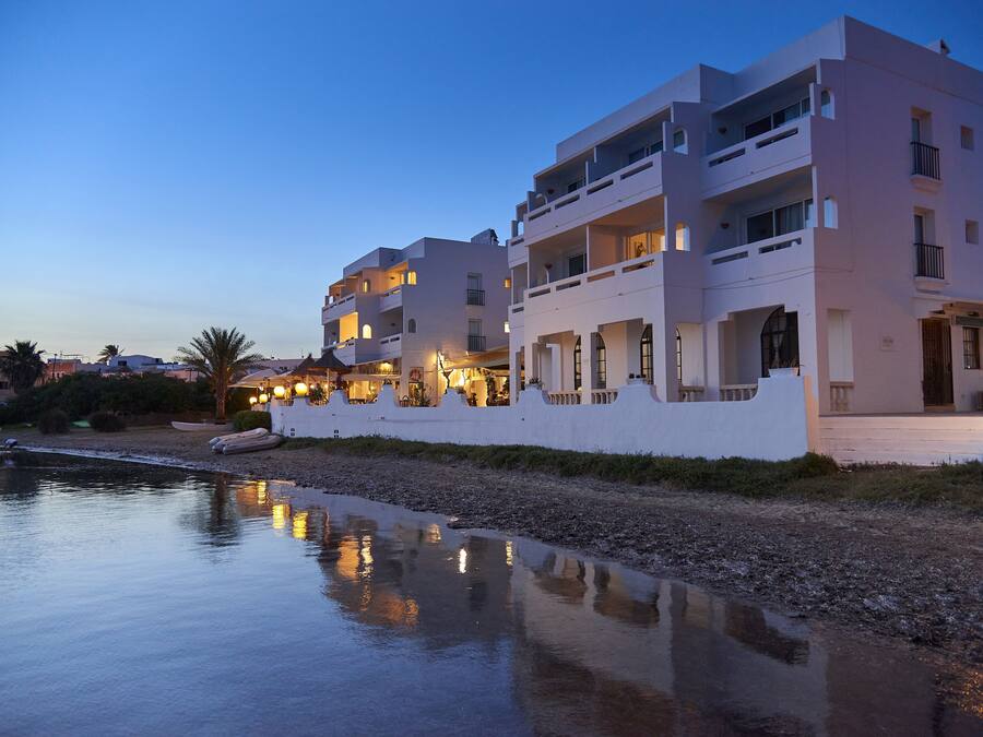 Un hotel frente al agua con varios balcones, piscina e iluminación exterior.
