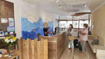 Un espace d’accueil avec un bureau en bois, une fresque murale et un coin salon avec un banc.