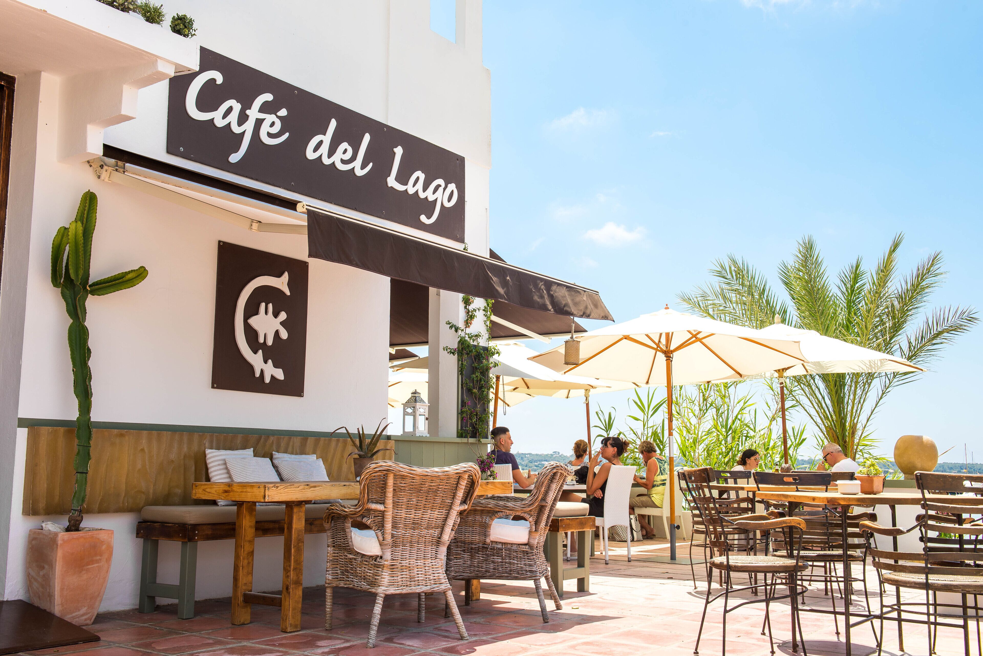 An outdoor café with wicker furniture and umbrellas, overlooking a scenic view.
