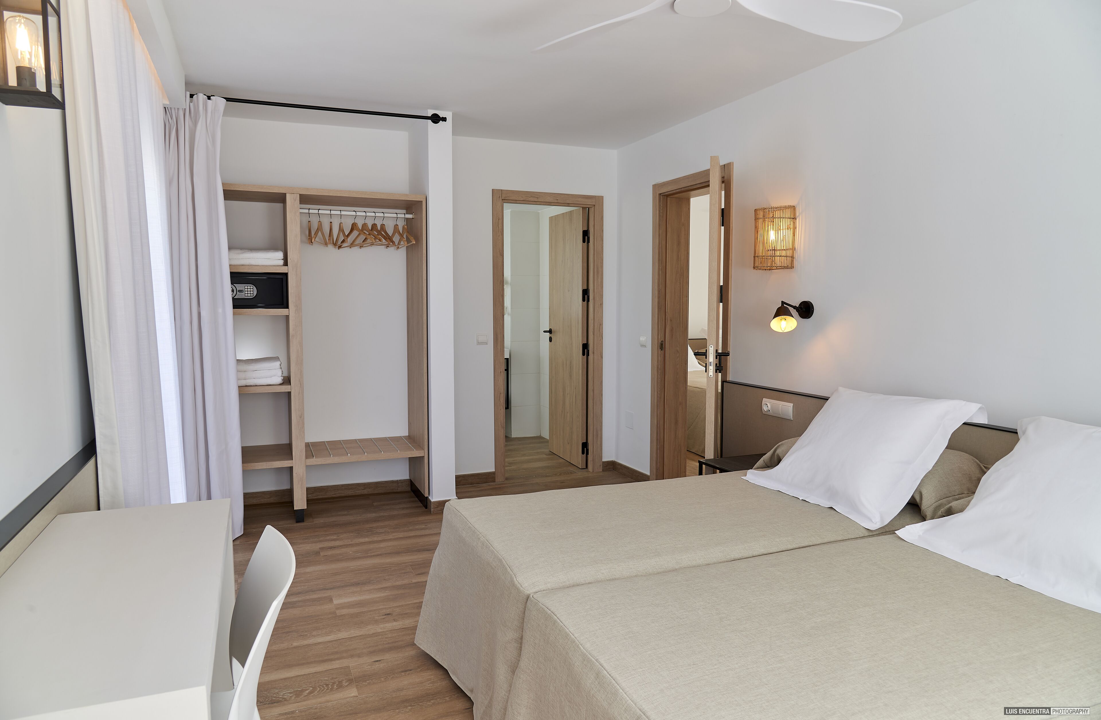 A hotel room with a bed, bedside table, chair, wardrobe, and a mirror.
