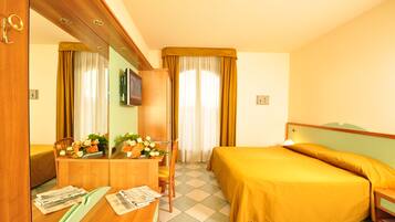 Ein Hotelzimmer mit Bett, Schreibtisch, Stuhl, Fernseher und Vorhängen.