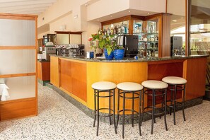 A bar area with a wooden counter, bar stools, and a variety of bottles and glasses. - Hotel Villa Elena (Tortoreto)