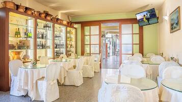 A hotel lobby with multiple tables and chairs, a wine display, and a television mounted on the wall.
