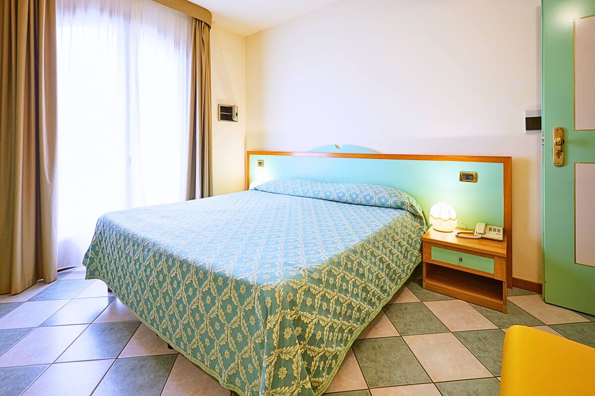 A hotel room with a bed, a nightstand with a lamp, and a green door.