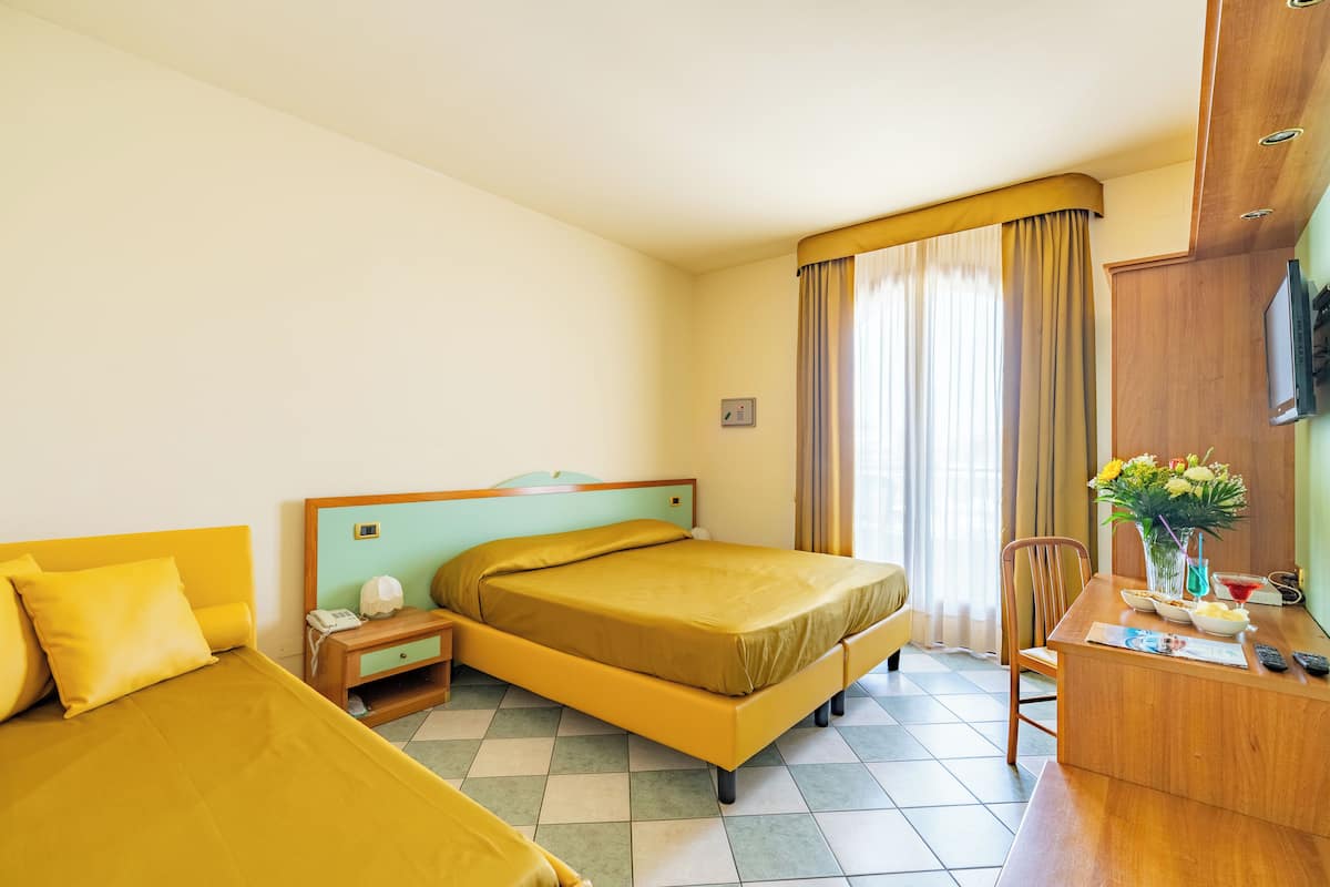 A hotel room with a bed, a desk with a chair, a TV, and a window with curtains.
