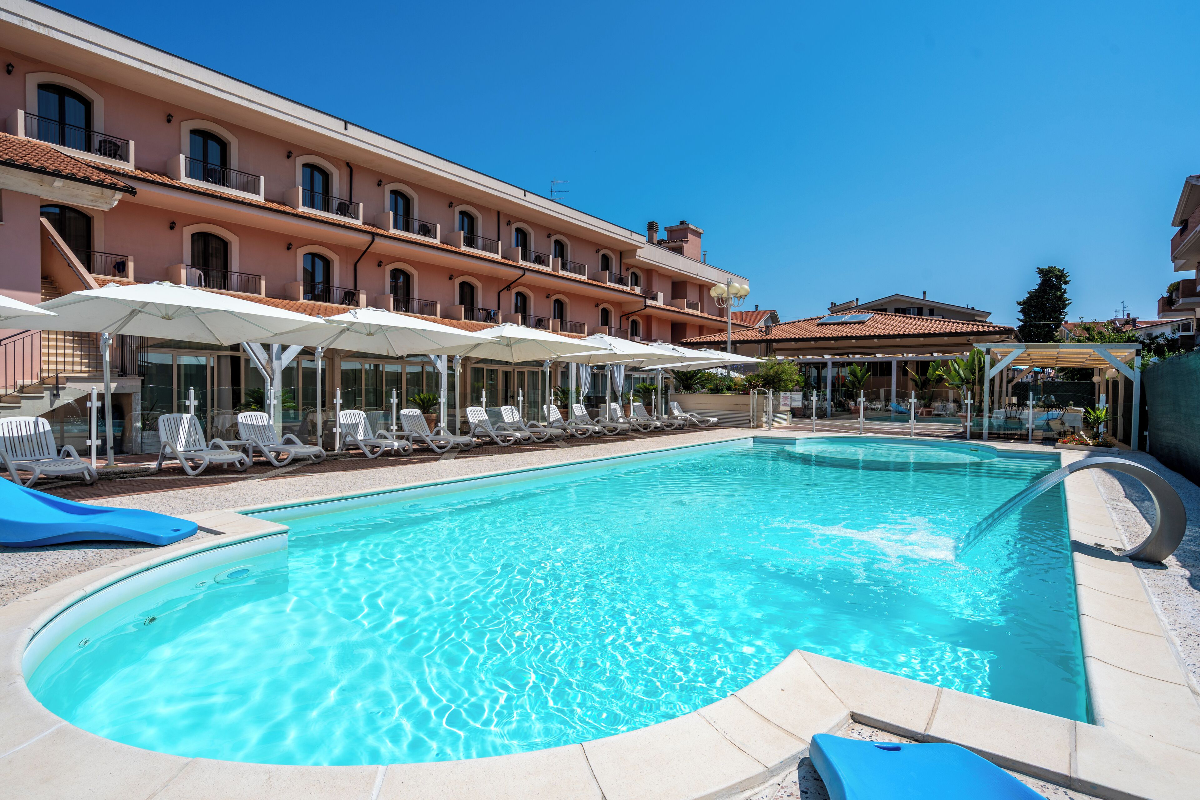 Une piscine entourée d’un bâtiment doté de balcons, avec des chaises longues et des parasols à proximité.