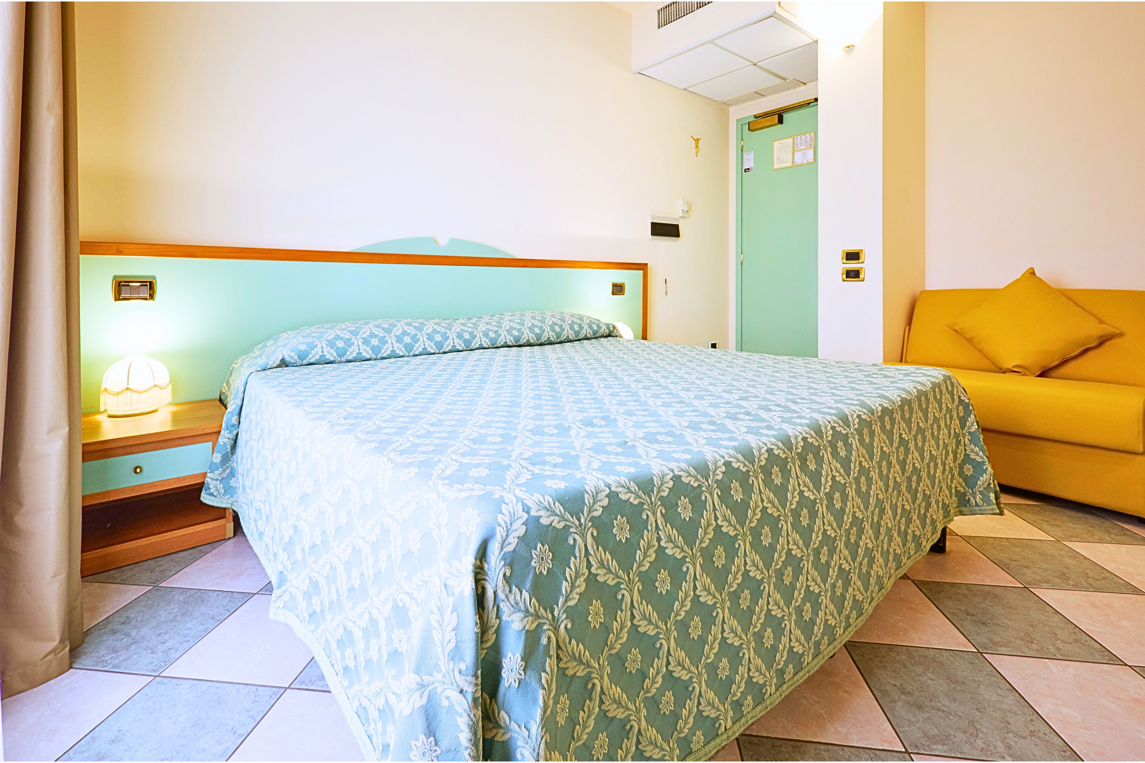 Un dormitorio con cama, mesita de noche, lámpara y sofá.