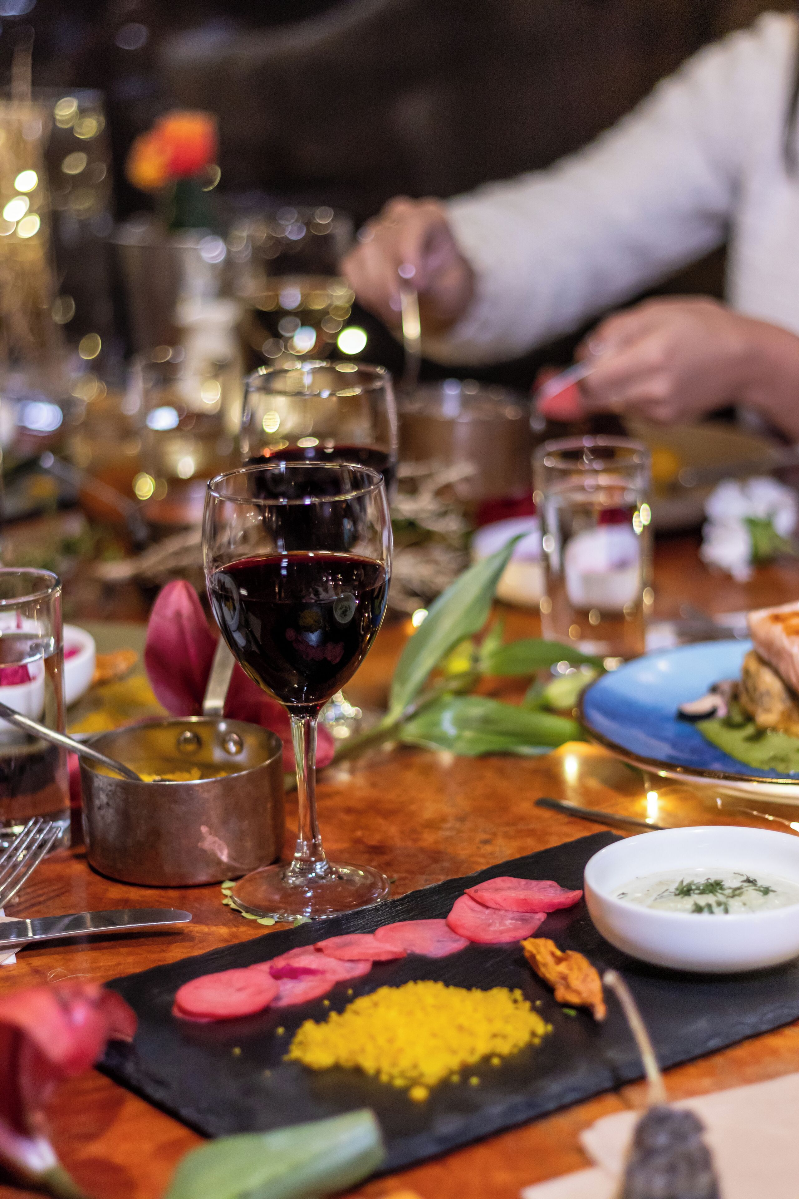 A dining table with a glass of red wine, a plate with food, and a bowl of sauce.