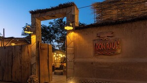 An entrance with a wooden archway, a sign reading "DON RAUL", and a stone wall with a thatched roof. - Don Raúl (San Pedro de Atacama)