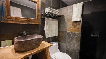 A bathroom with a stone sink, white toilet, and a shower area.
