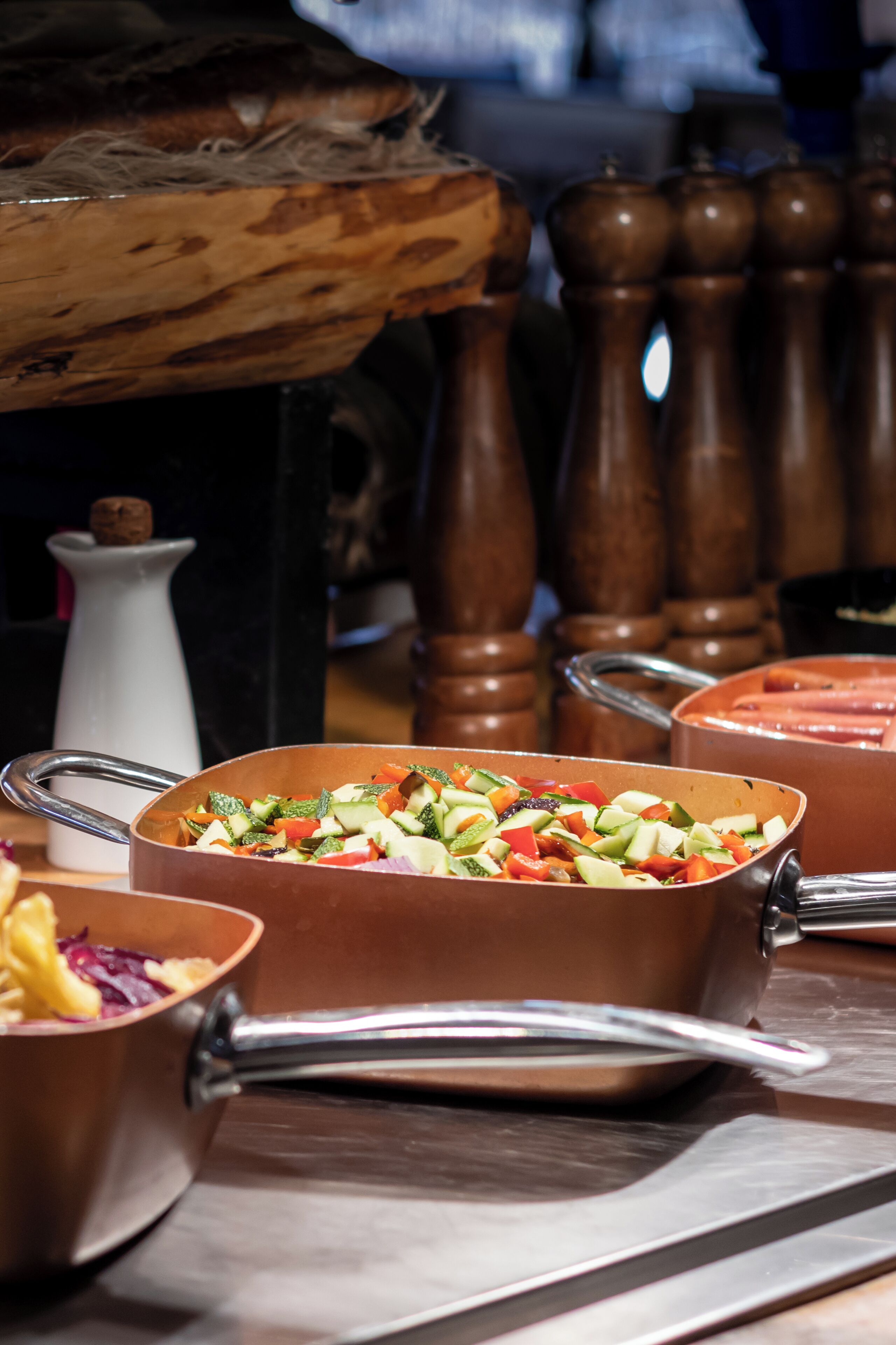 A kitchen with a large copper pan filled with diced vegetables, a white pitcher, and wooden salt and pepper shakers.