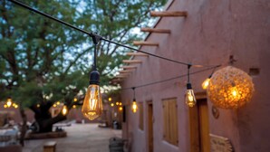 A string of hanging light bulbs in an outdoor setting with a building in the background. - Don Raúl (San Pedro de Atacama)