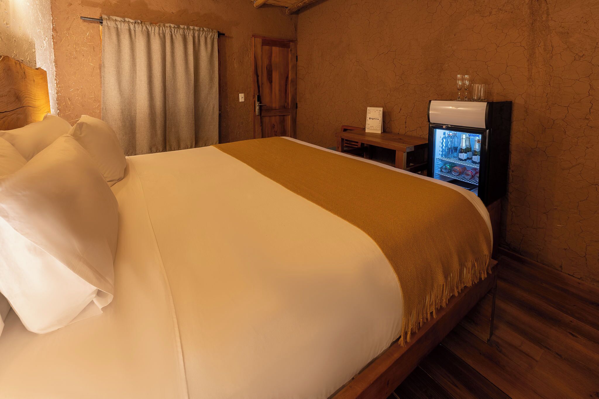 Une chambre d’hôtel avec un grand lit, une tête de lit en bois, un minibar et un plancher en bois.