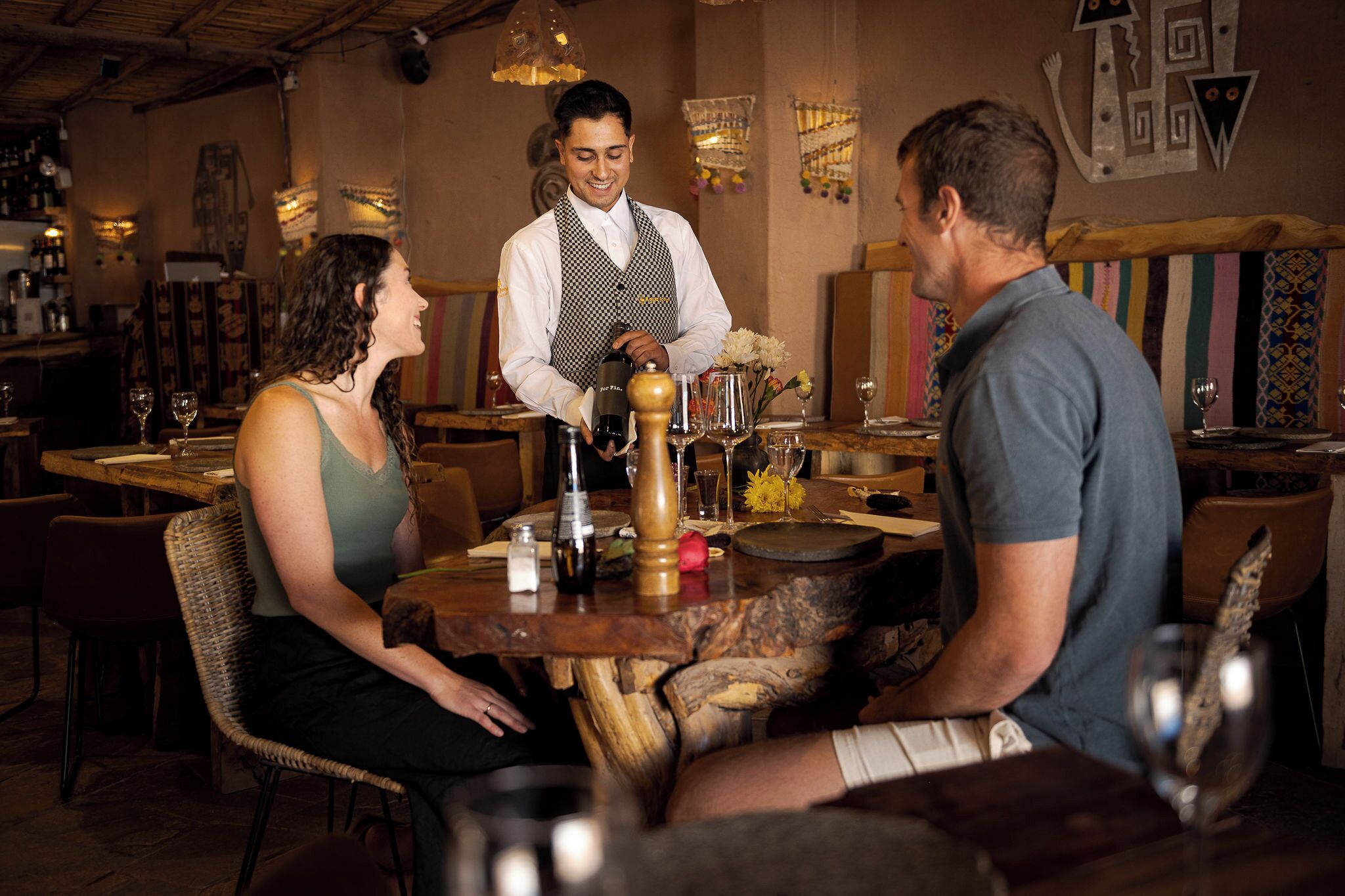 A restaurant interior with wooden tables, wicker chairs, and hanging light fixtures.